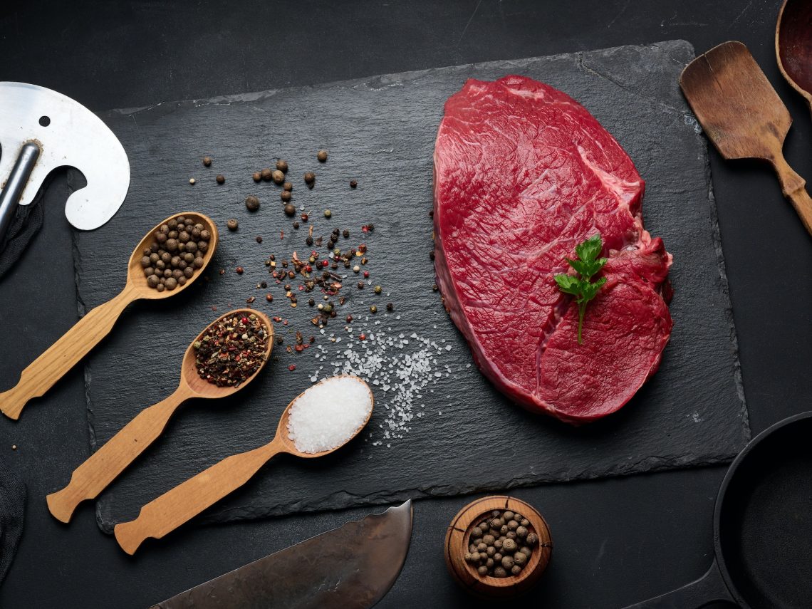 Raw beef tenderloin lies on a board, black table.