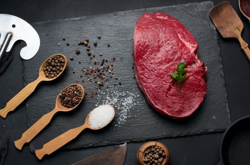 Raw beef tenderloin lies on a board, black table.