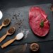 Raw beef tenderloin lies on a board, black table.